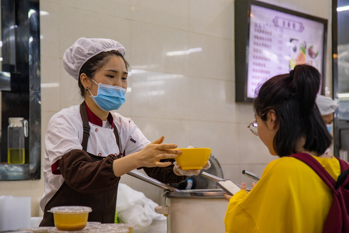 双手向点餐的同学递送粥品（学通社记者 徐剑锋 摄）